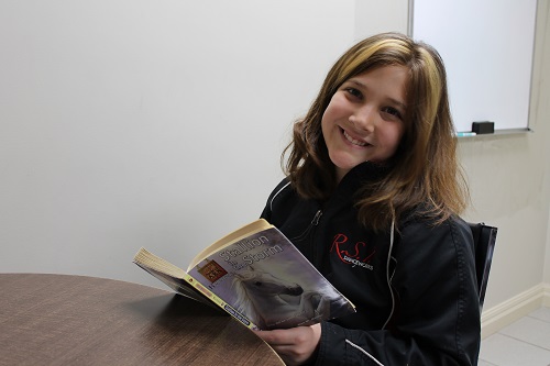 A photo of a smiling young student learning to read and understand language at Foundations for Learning